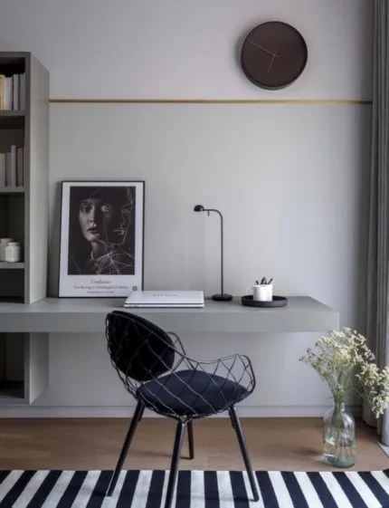 Minimalistická pracovna s deskou u stěny, černou židlí a pruhovaným kobercem