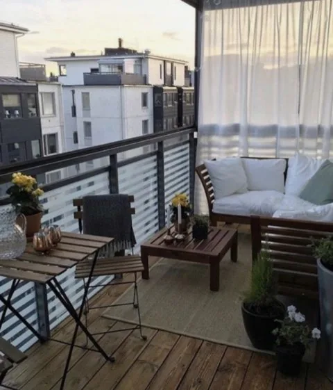 Balkon s dřevěným nábytkem a průsvitnými závěsy nad městem