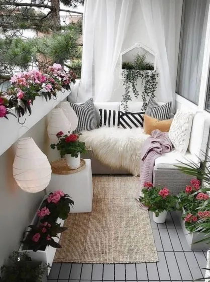 Balkon se závěsy, bílou lavicí a truhlíky s muškáty
