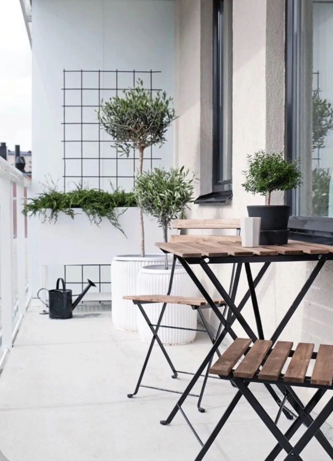 Malý balkon se skládacím stolkem, židlemi a olivovníky v květináčích