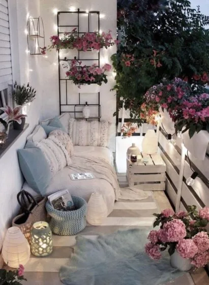 Útulný balkon s polštáři, květinami a lampiony ve večerním osvětlení